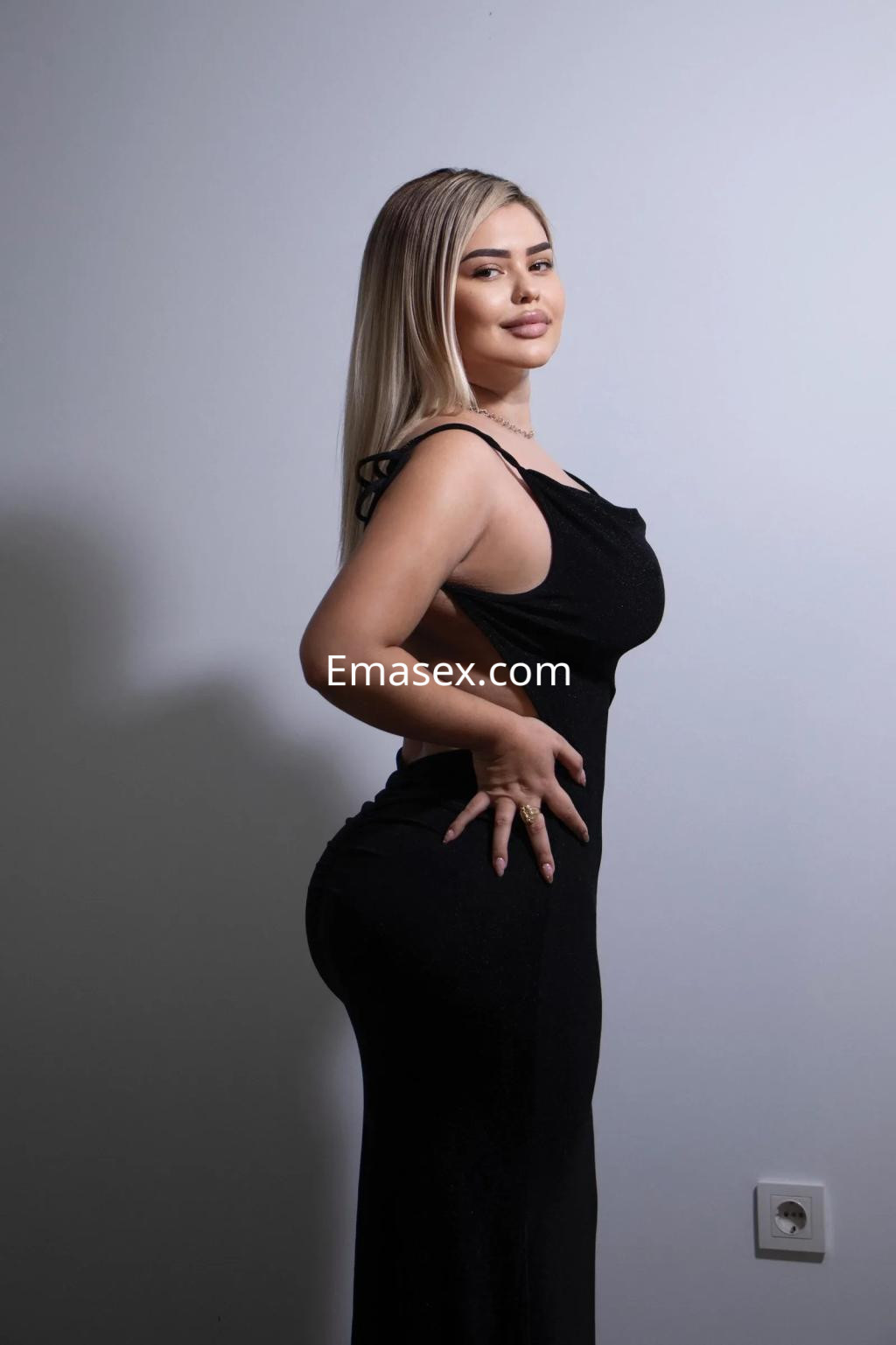 Escort en Cádiz vestida con un ajustado vestido negro, posando de perfil con cabello largo y rubio.