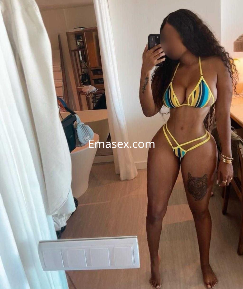 Puta con cabello rizado y oscuro, viste un bikini de rayas amarillas y posando en un espejo en Granada.