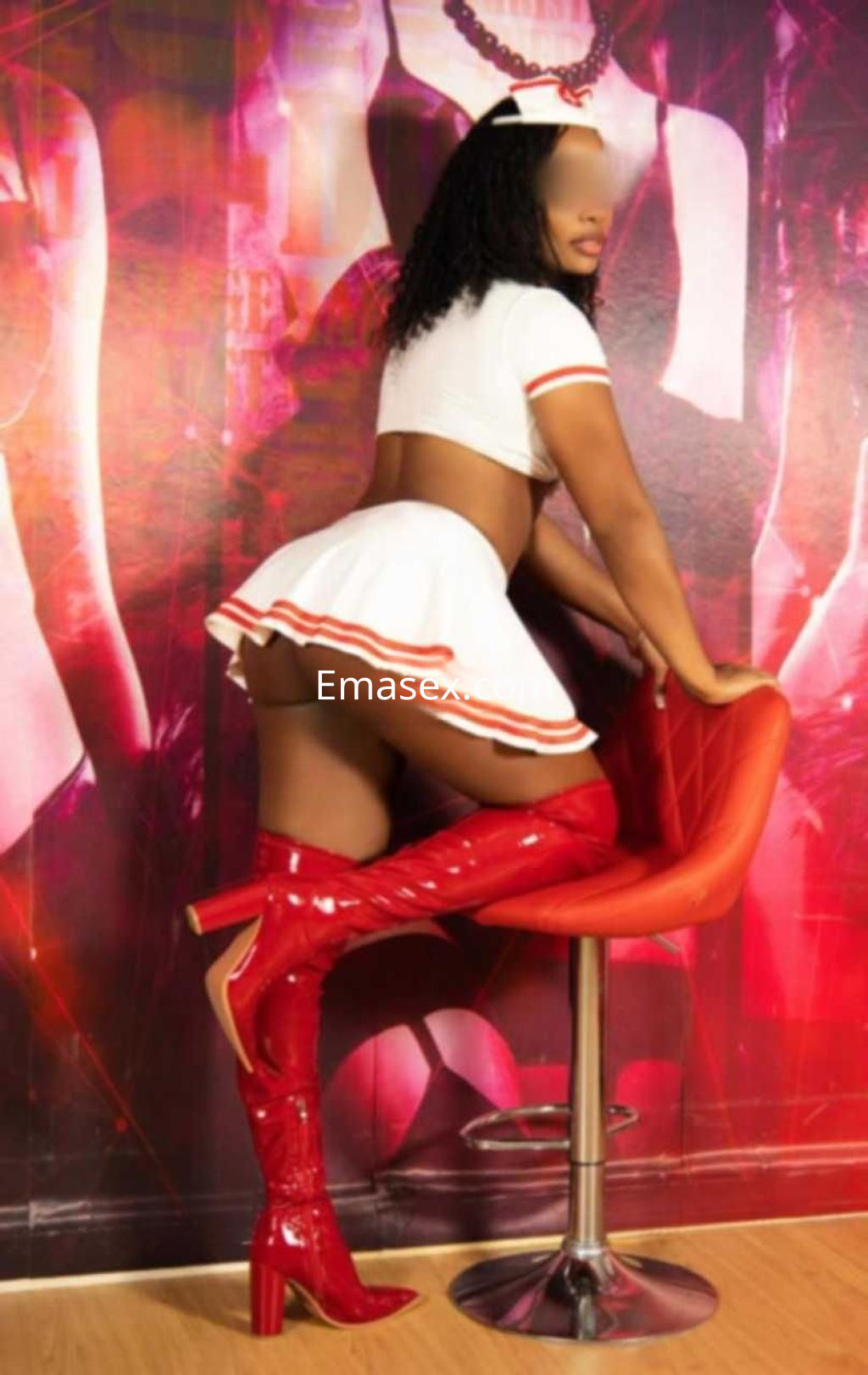 Escort en Zaragoza con cabello rizado y oscuro, vestida con un atuendo de enfermera y botas rojas, posando en una silla.