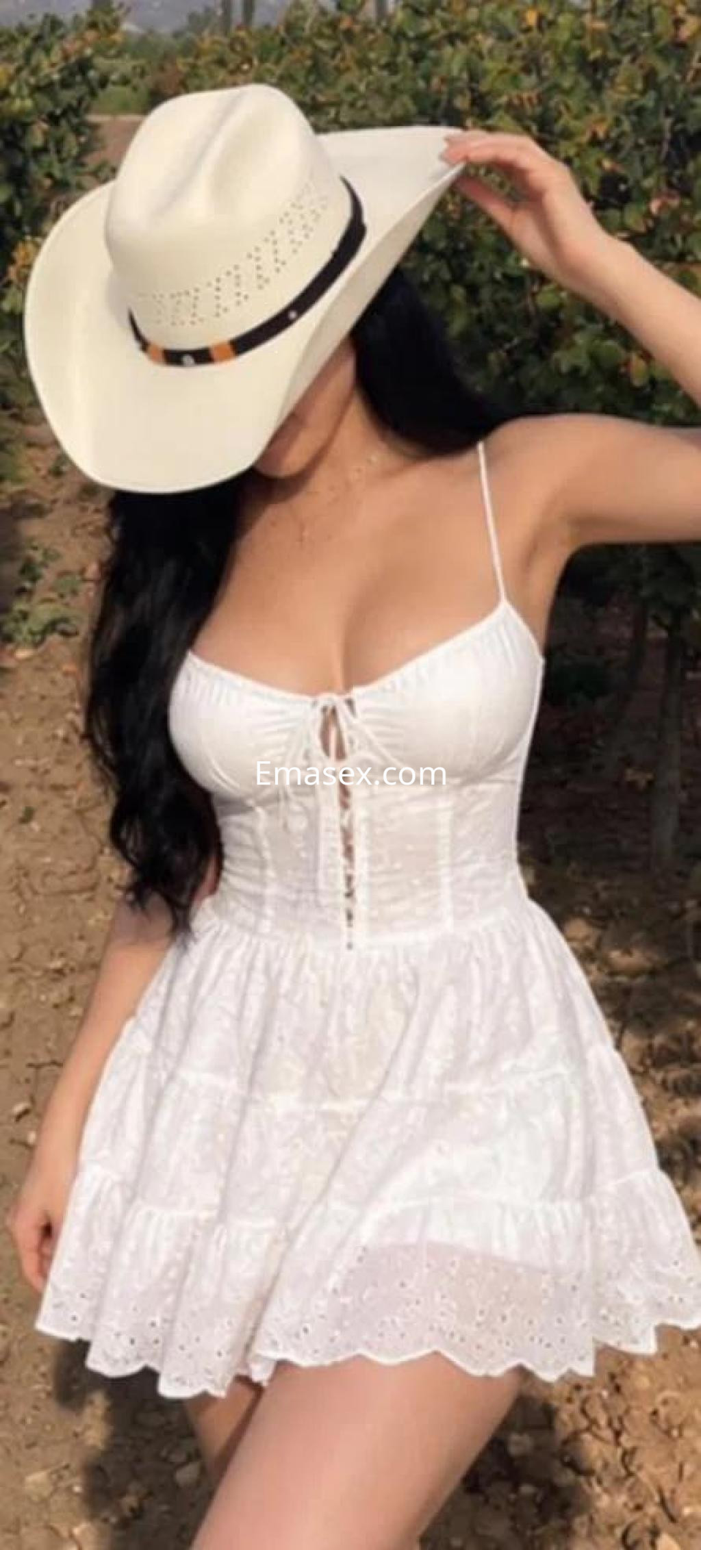 Escort en Murcia luciendo un vestido blanco con detalles y un sombrero, posando en un entorno natural.