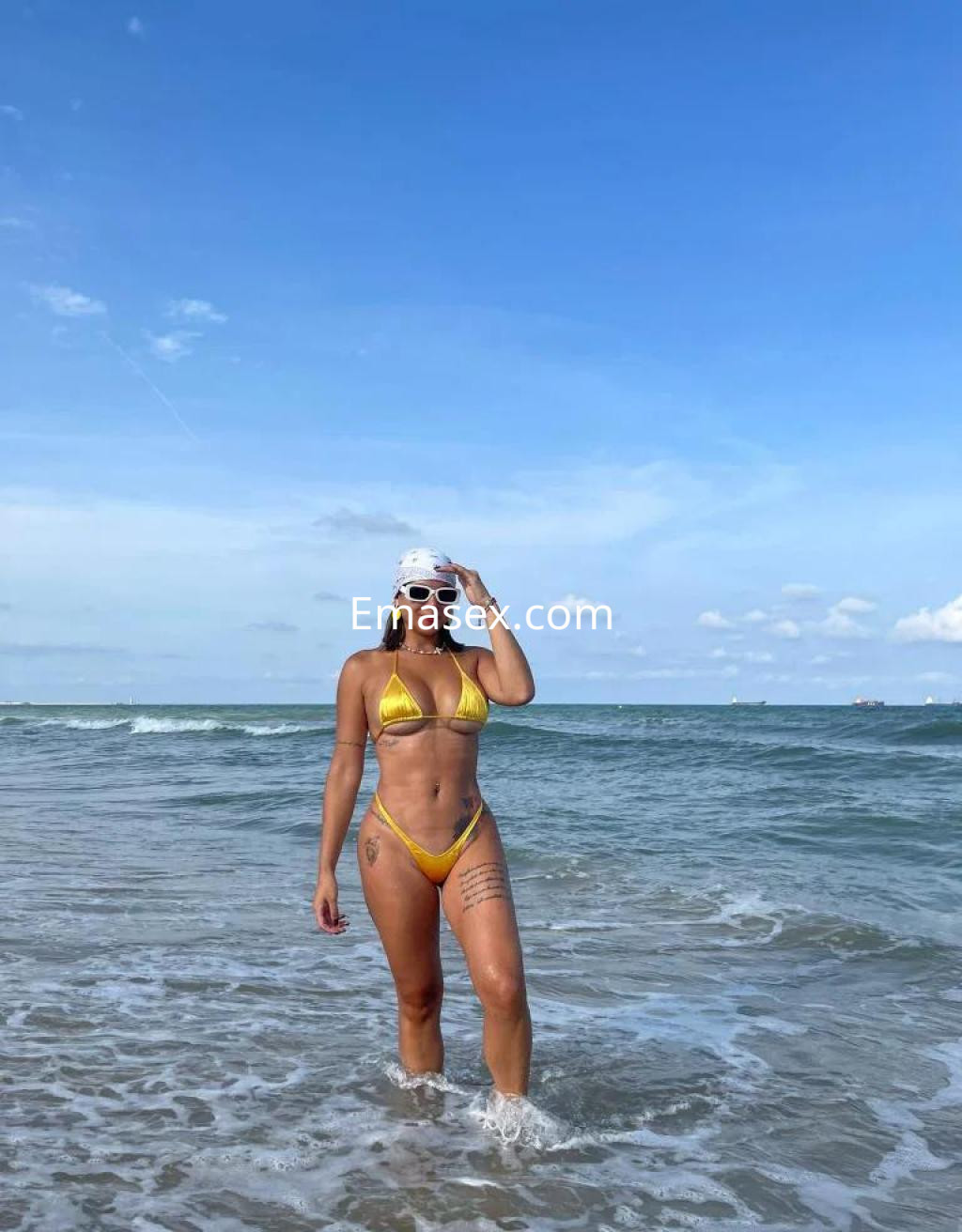 Puta en Palma de Mallorca, luciendo un bikini amarillo mientras camina por la playa con el mar de fondo.
