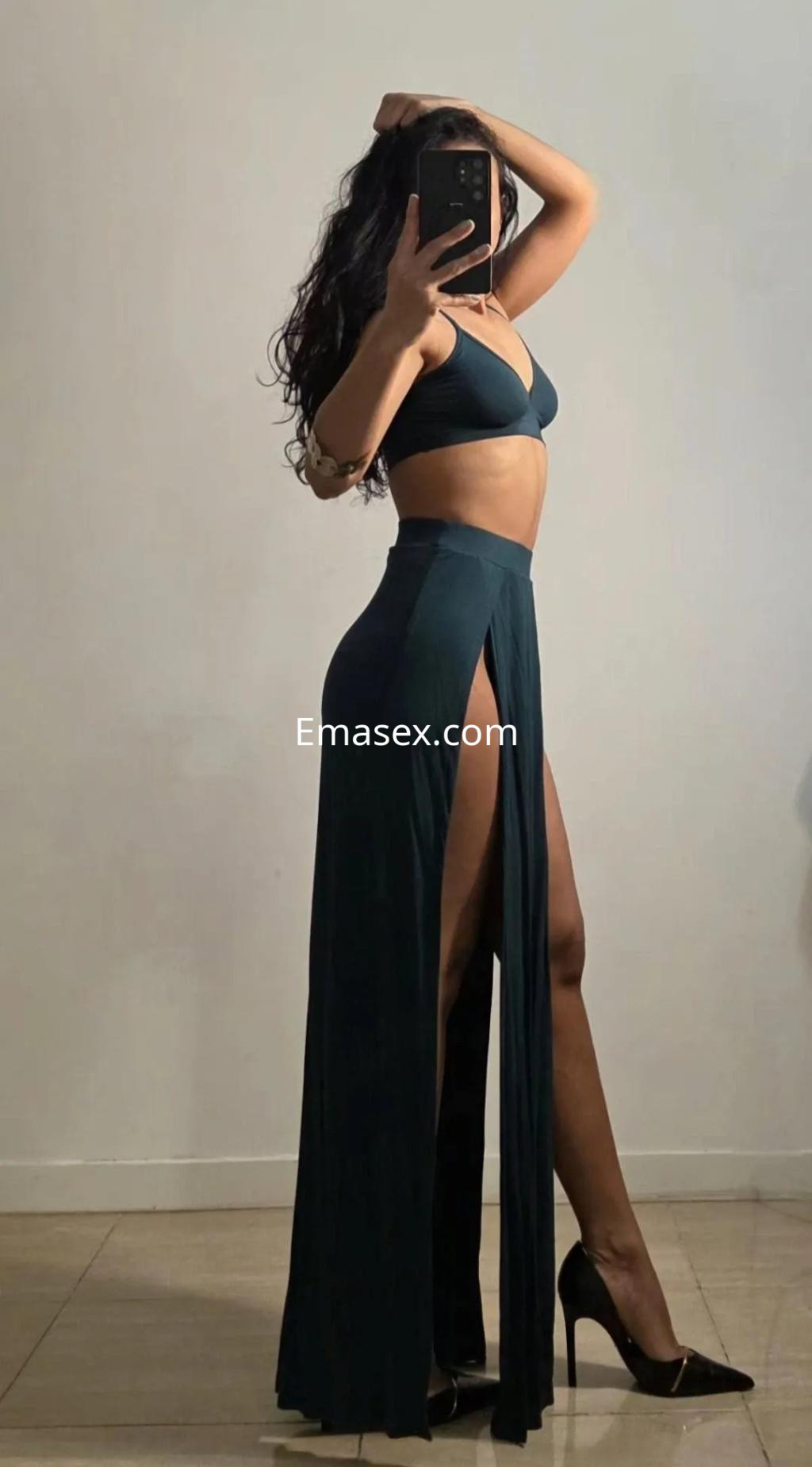 Escort en Palma de Mallorca, luciendo un conjunto de dos piezas verde y una falda larga con abertura, en pose lateral.