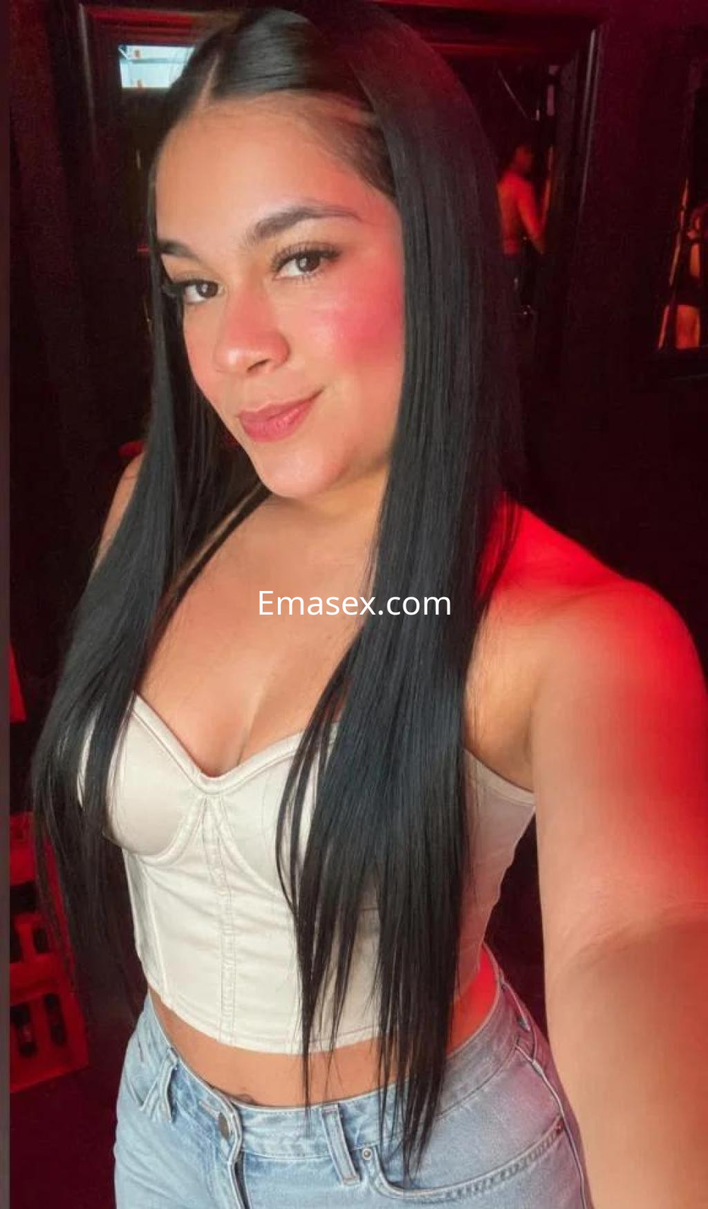 Escort en Tenerife con cabello largo y lacio, lleva un top claro y jeans, posando con una sonrisa.