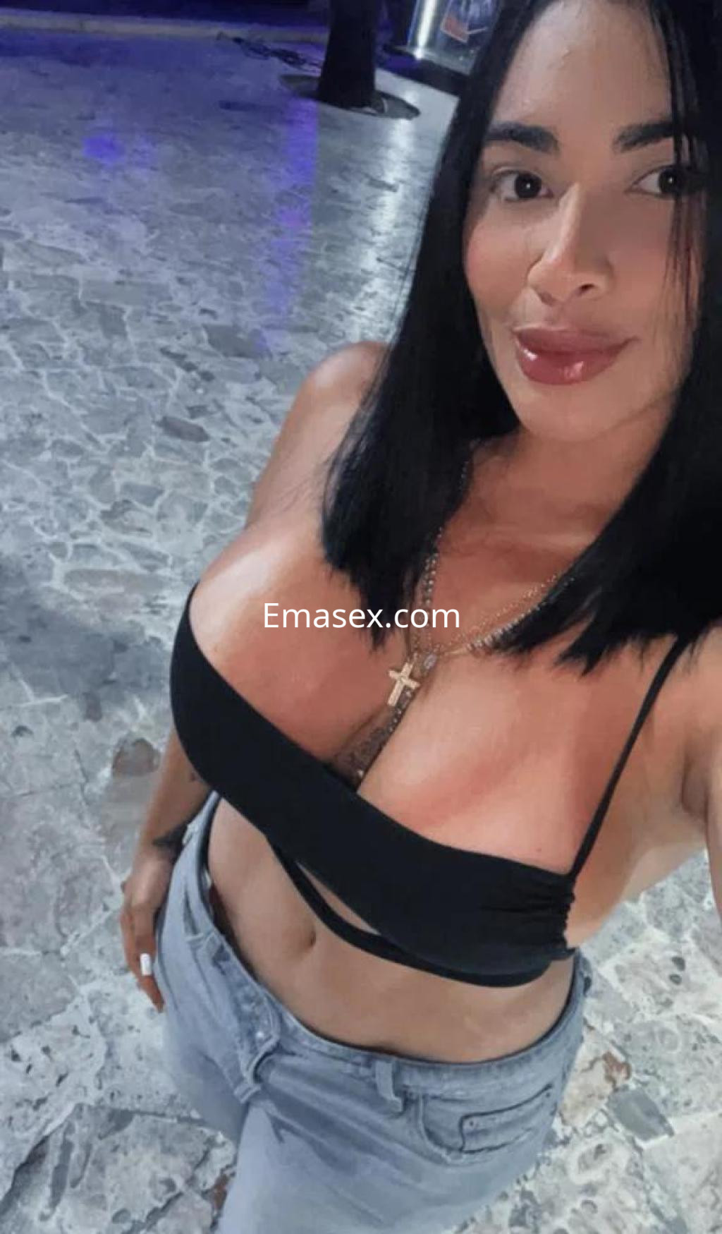 Puta en Tenerife, luciendo un top negro y jeans ajustados, con cabello oscuro y lacio en un ambiente nocturno.