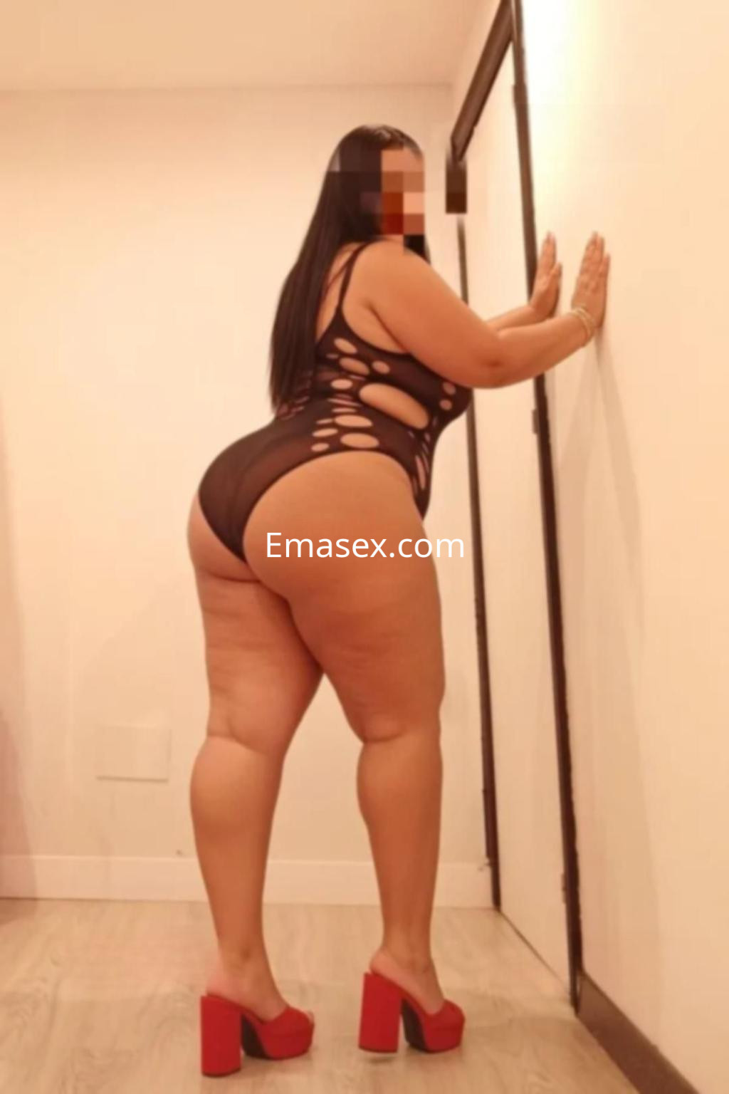 Puta de pie en un ambiente interior, vistiendo un body negro con detalles recortados y tacones rojos en León.