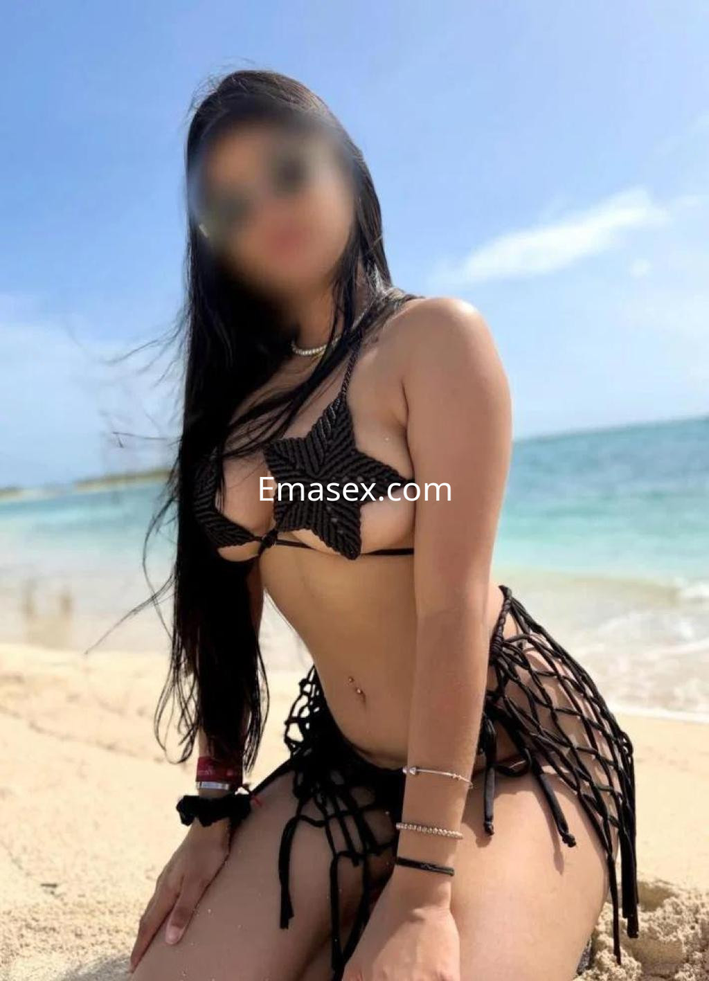 Puta posando en la playa de Murcia, vistiendo un bikini negro con detalles, con el mar y el cielo de fondo.