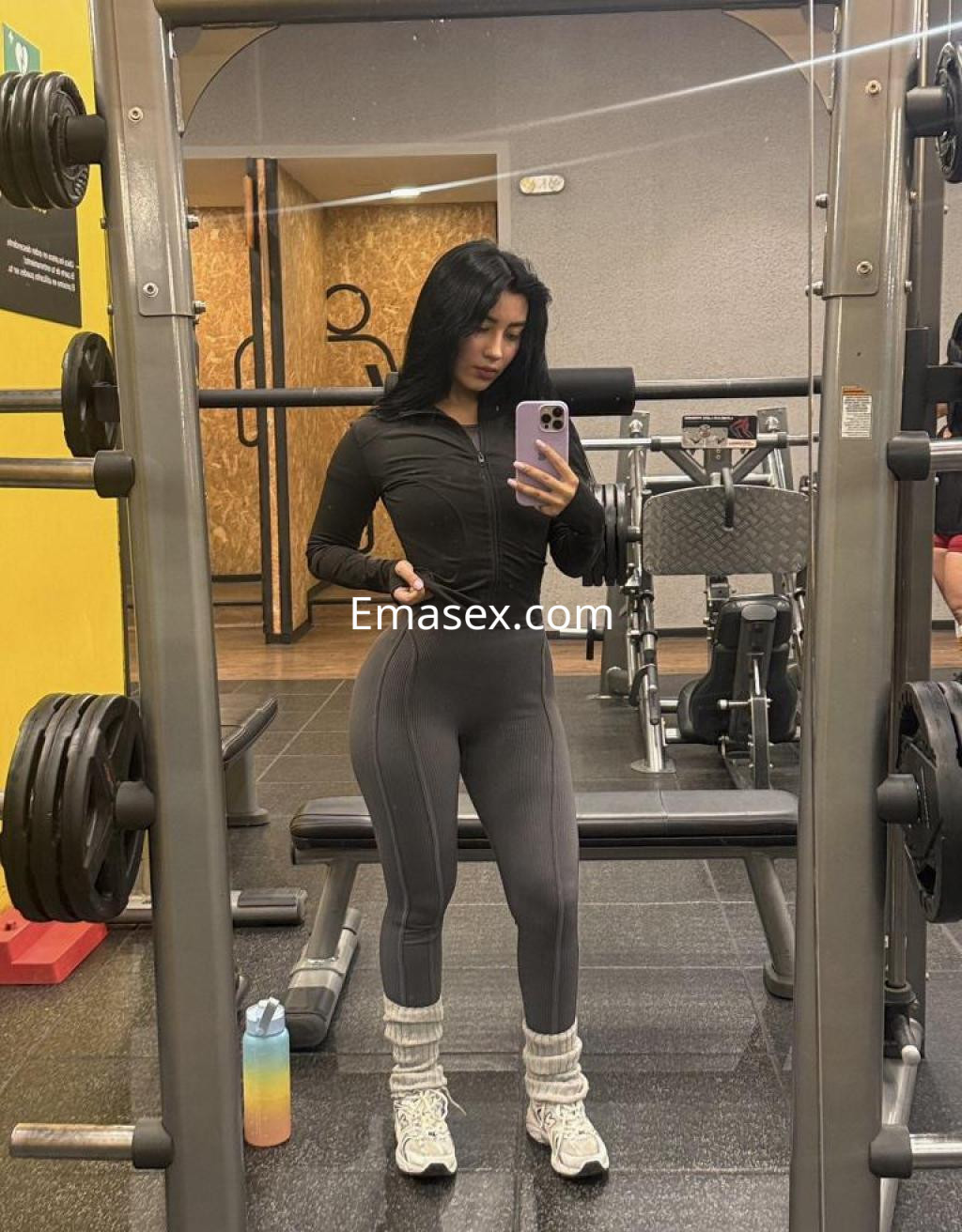 La puta luce un conjunto deportivo negro con mallas ajustadas, posando en un gimnasio moderno en Murcia.
