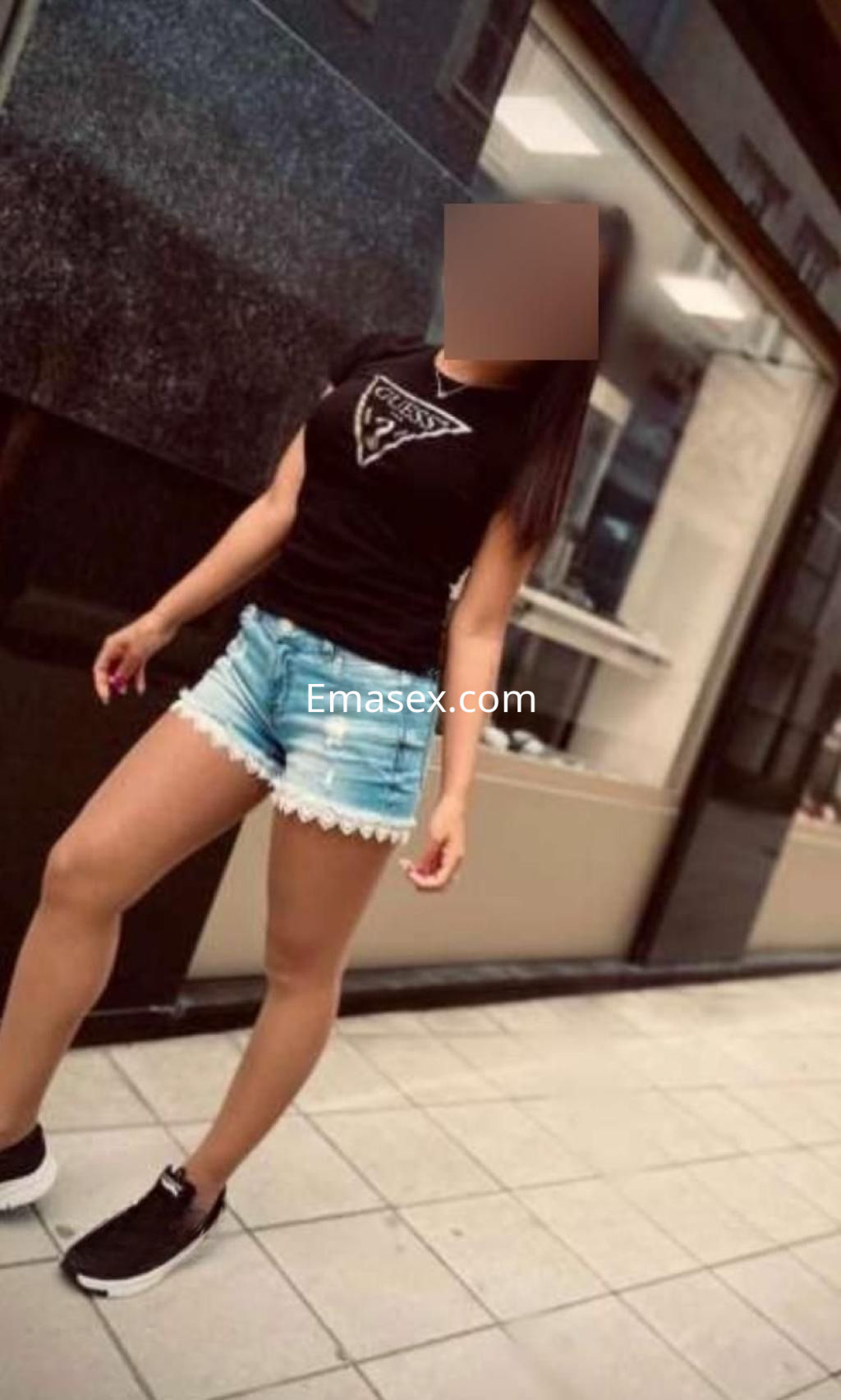 Escort en Madrid con camiseta negra y pantalones cortos de mezclilla, posando de pie en una calle.
