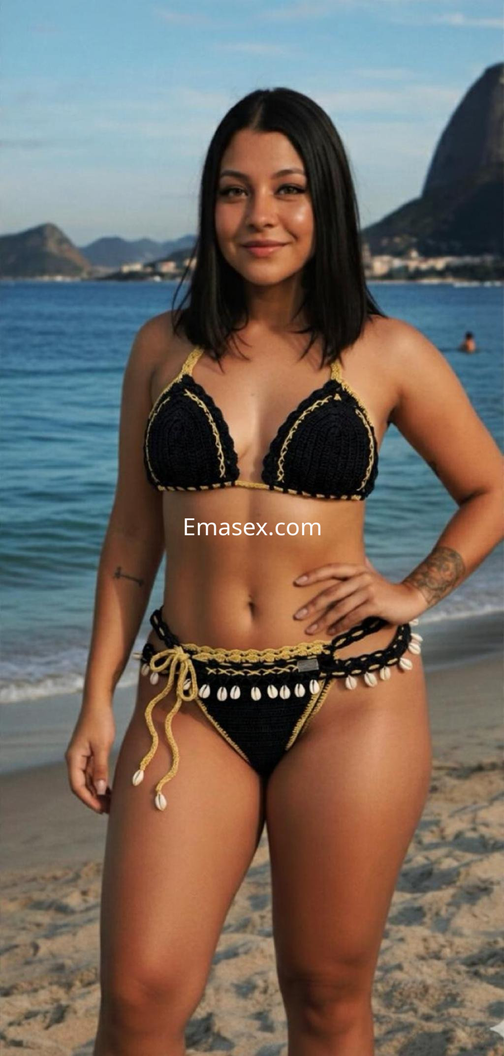 Escort en Pamplona en la playa, luciendo un bikini negro con detalles en dorado y con el mar de fondo.