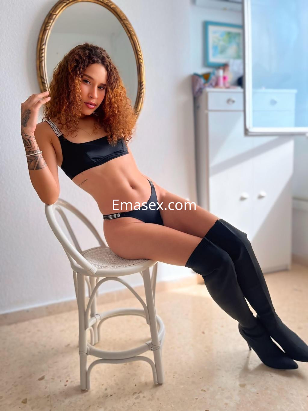 La puta se presenta sentada en una silla, luciendo una lencería negra y botas altas en Granada.