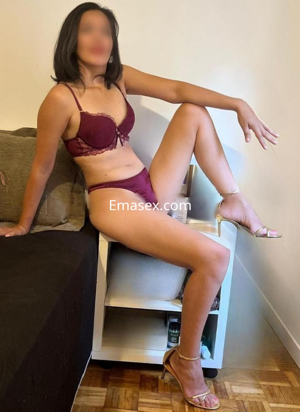 Escort en Madrid sentada sobre una silla, con lencería burdeos y tacones dorados, mostrando una pose elegante.