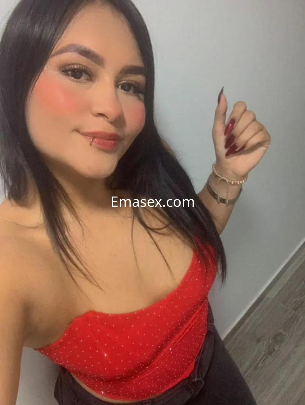 Escort en Toledo con blusa roja sin mangas, cabello largo y lacio, posando con una mano levantada.