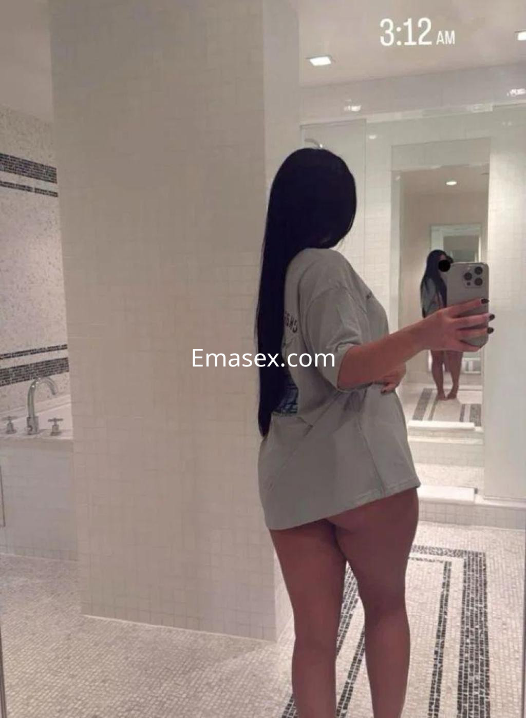 Escort en Murcia, con cabello largo y lacio, viste una camiseta oversize en un baño moderno.