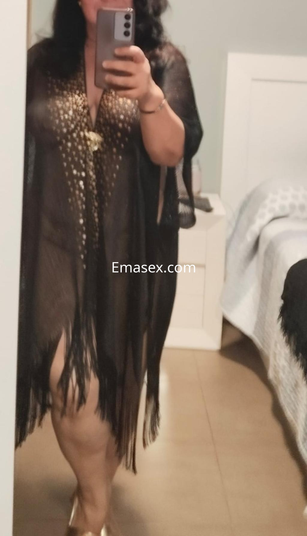 Puta en Pontevedra luciendo un kimono negro con detalles dorados y flecos, posando frente a un espejo.