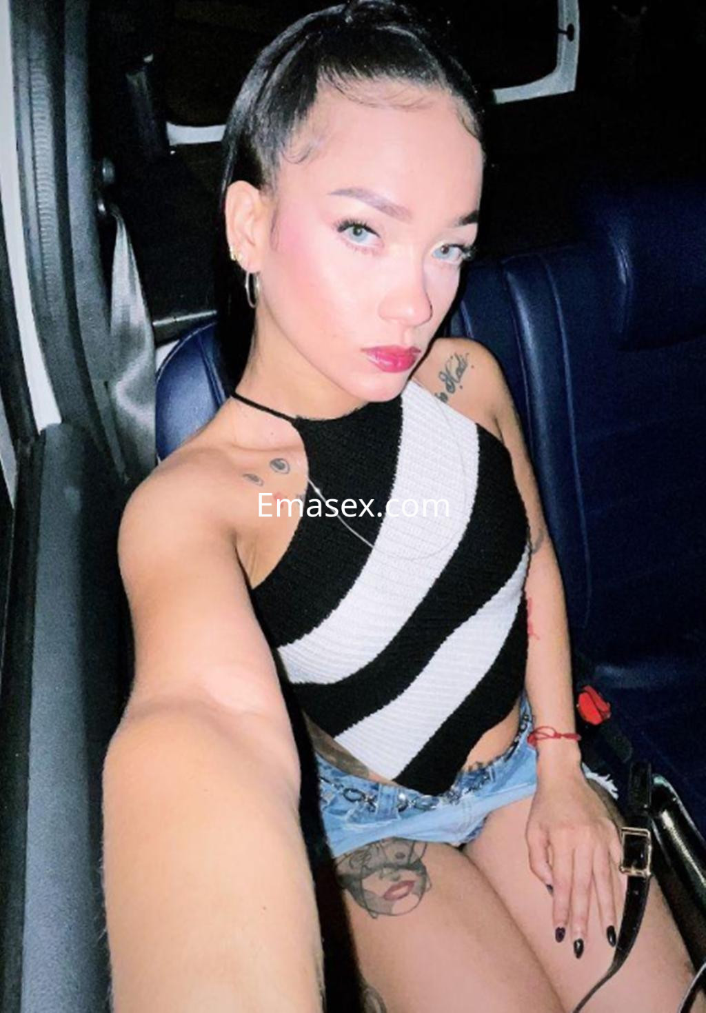 La escort en Gijón se toma un selfie en un coche, vistiendo un top de rayas y shorts de mezclilla.