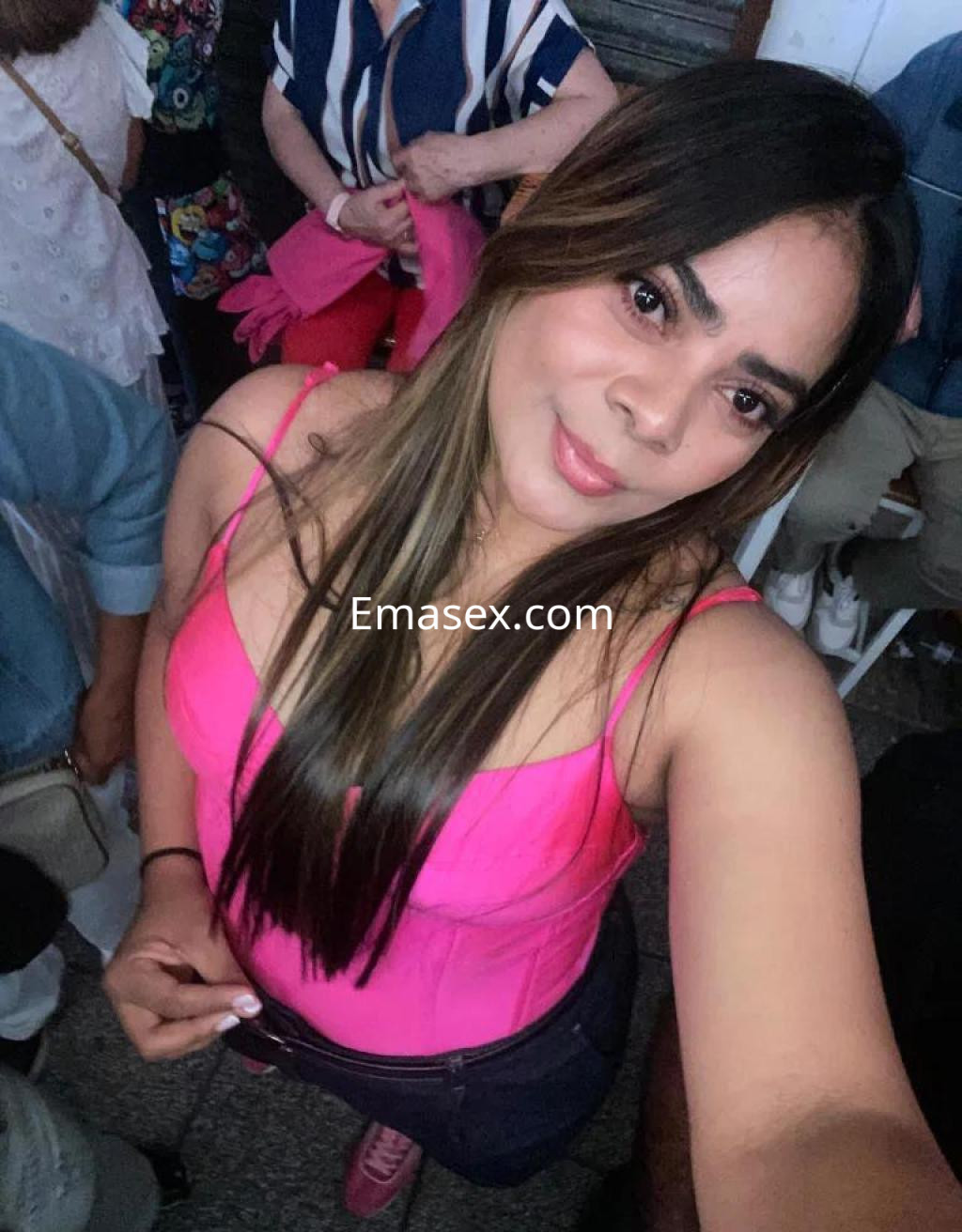 Escort en Sevilla posando con una blusa rosa ajustada, cabello largo y lacio, en un entorno social.