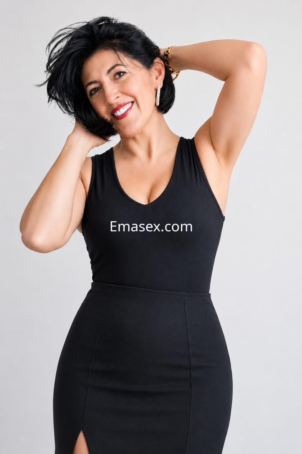 Escort en Madrid, con cabello corto y oscuro, viste un vestido negro ajustado mientras sonríe y se acaricia el pelo.