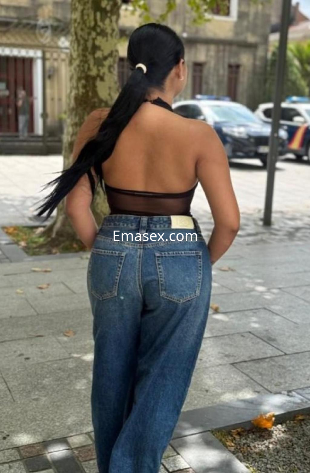 Escort en Zaragoza con top transparente y jeans ajustados, de espaldas, caminando por la calle.