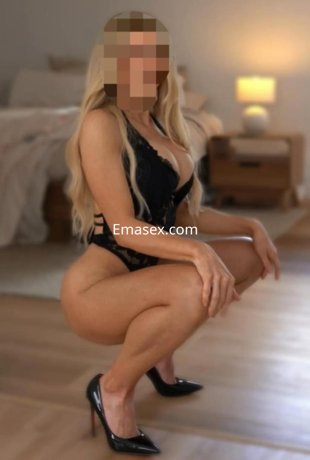 Escort en Coruña, vistiendo un body de encaje negro y tacones altos, posando en un ambiente moderno y luminoso.