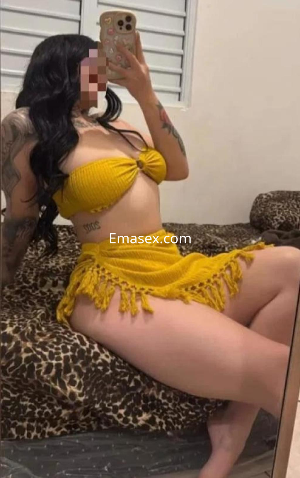 Escort en Madrid se muestra en un espejo, luciendo un bikini amarillo y una falda corta, con cabello largo y ondulado.