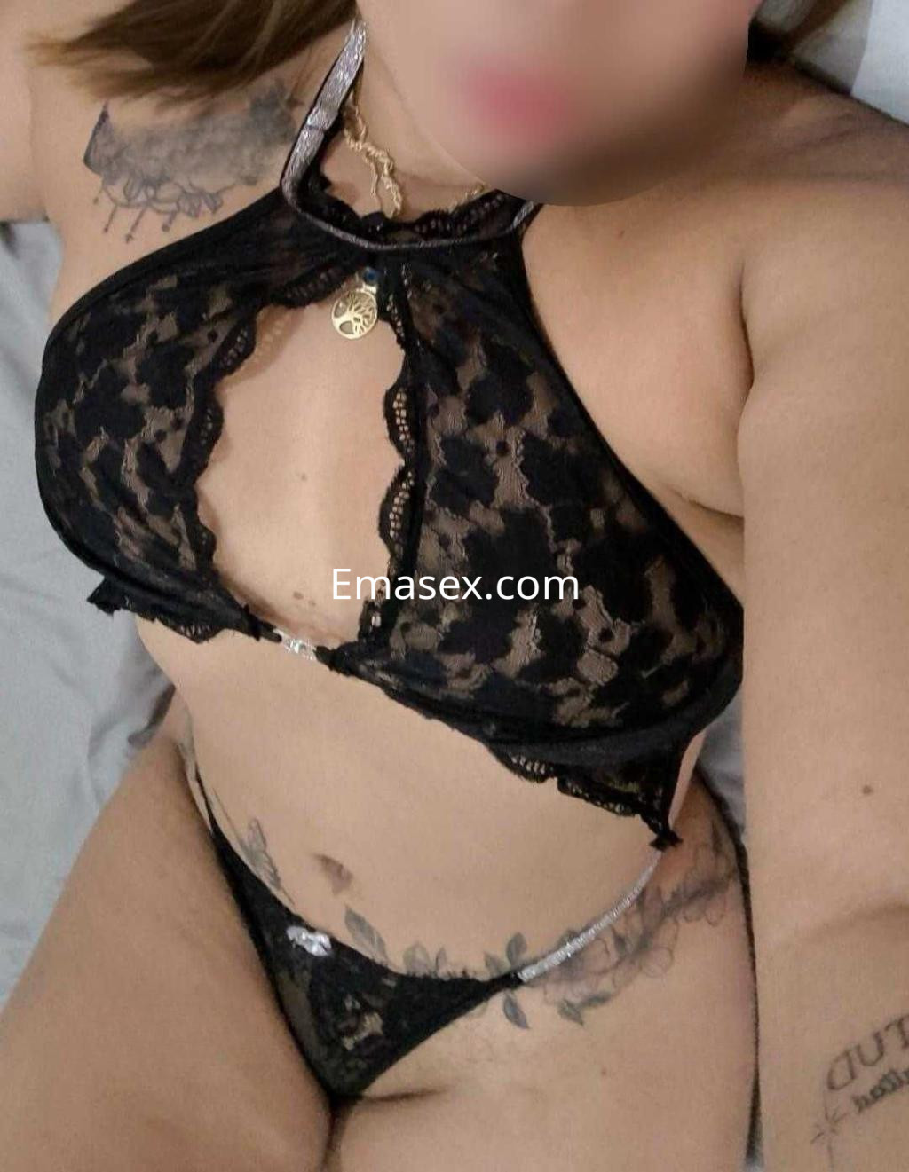 La escort en Madrid viste un conjunto de lencería negra de encaje con detalles brillantes y luce varios tatuajes en su piel.