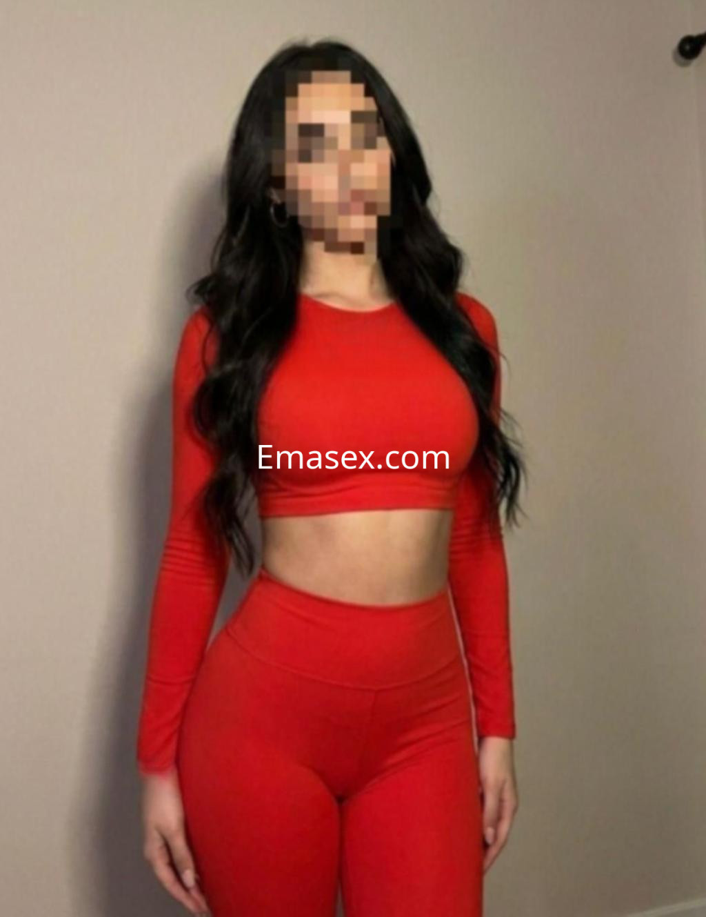 La escort posa de pie en Madrid, vistiendo un conjunto rojo de top ajustado y leggings que resaltan su figura.