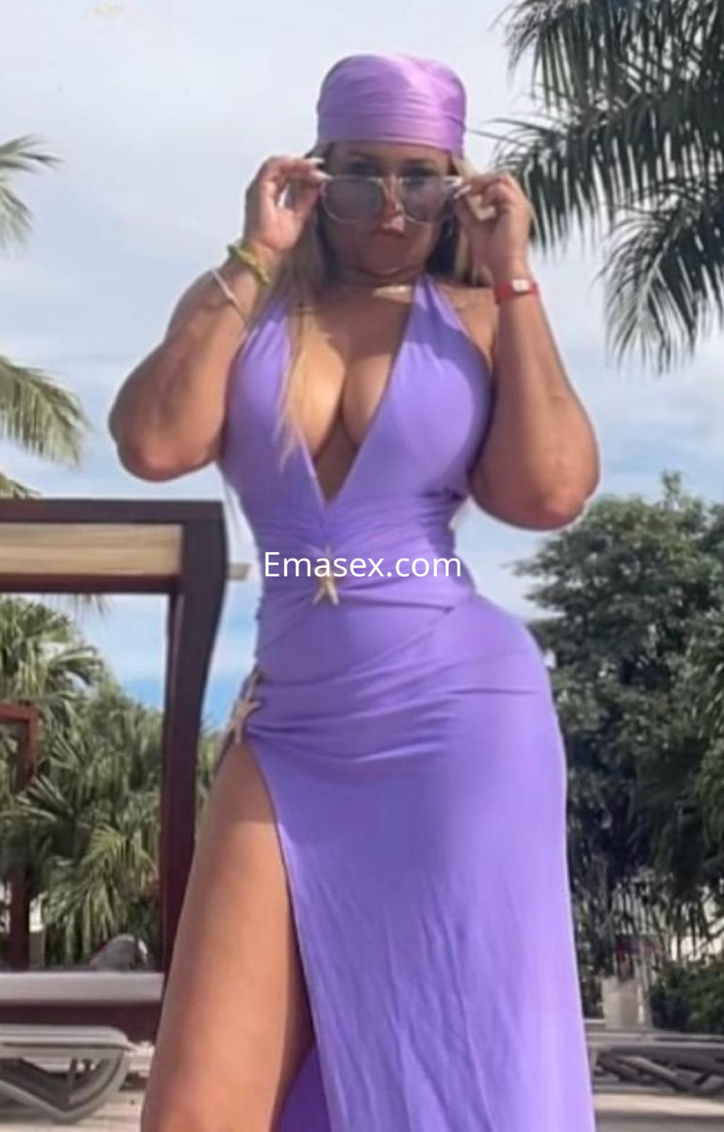 Escort en Madrid con cabello recogido y vestido morado ajustado, posando con gafas de sol en un ambiente al aire libre.