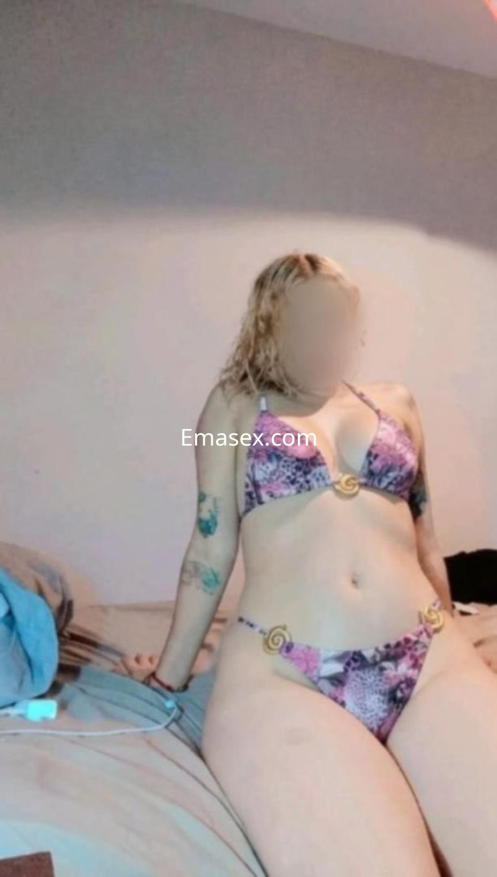 Escort en Murcia luciendo un bikini de estampado floral, sentada en una cama con una postura relajada.