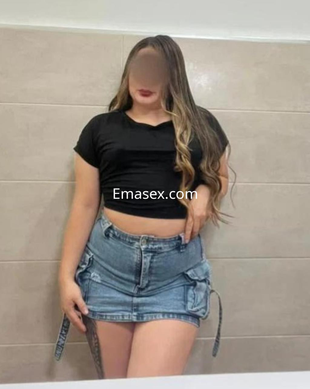 Puta en Madrid, con cabello largo y ondulado, viste una blusa negra ajustada y una falda de mezclilla corta.