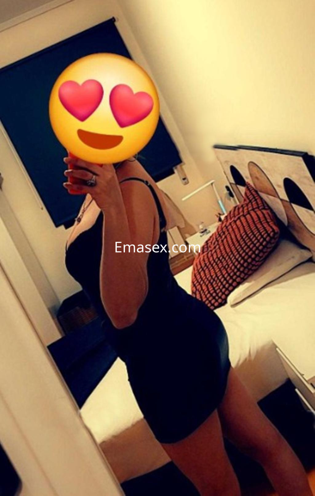 Escort en Valladolid posando de lado con vestido negro ajustado en un ambiente interior acogedor.