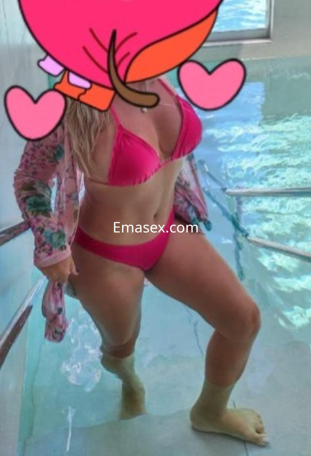 Escort en Burgos con cabello rubio y lacio, usando un bikini rosa y un kimono floral, entrando a una piscina.