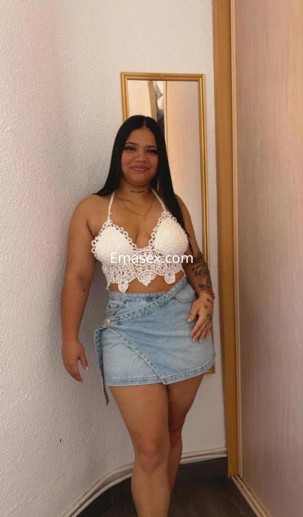 Escort en Madrid posando con blusa blanca de encaje y falda de mezclilla, cabello largo y lacio.
