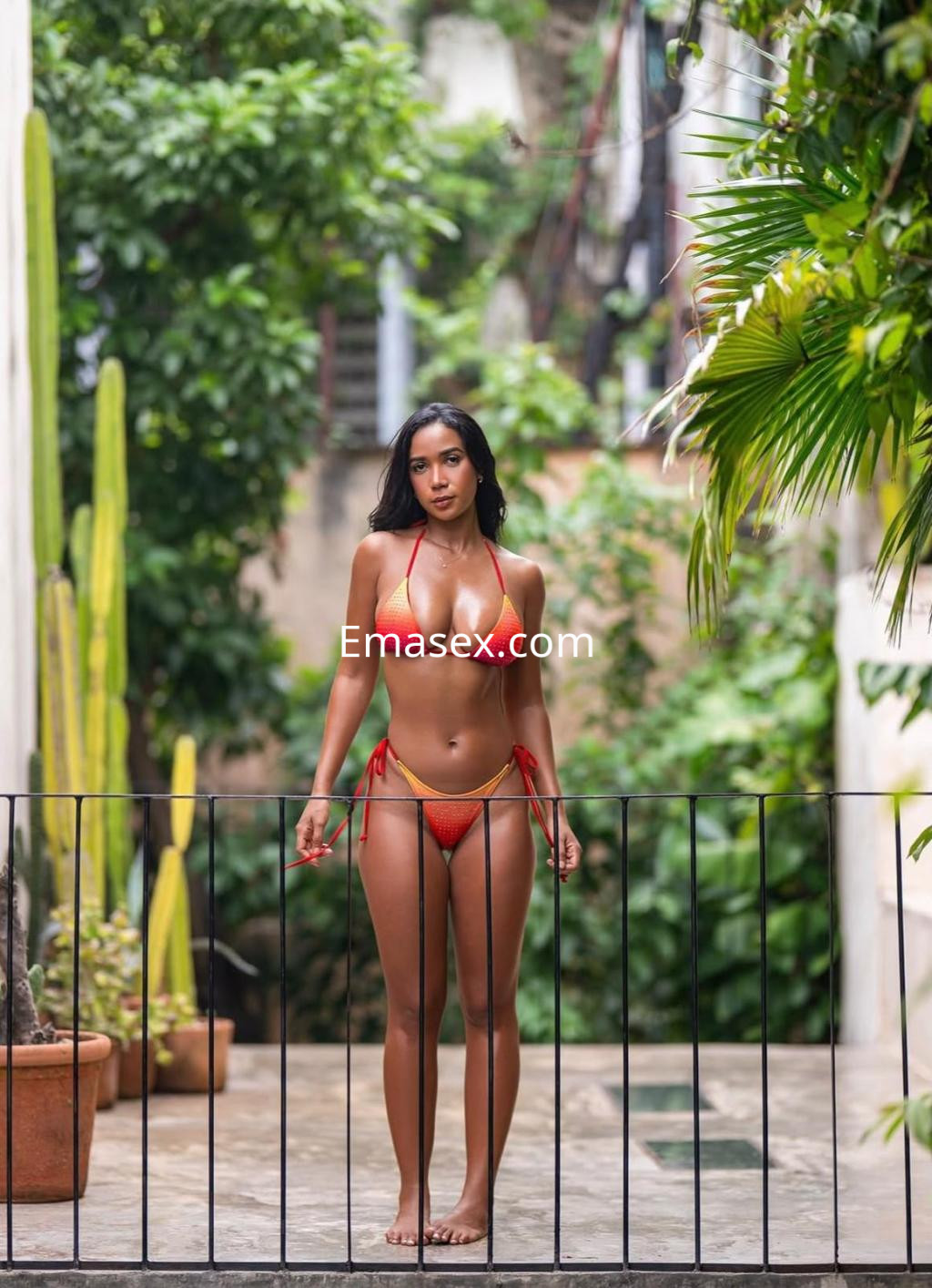 Escort en Santander, de pie en un entorno verde, luciendo un bikini rojo que resalta su figura.