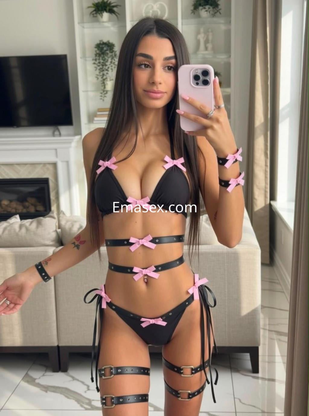 Escort en Santander posando con un bikini negro adornado con lazos rosas, en un ambiente moderno y luminoso.