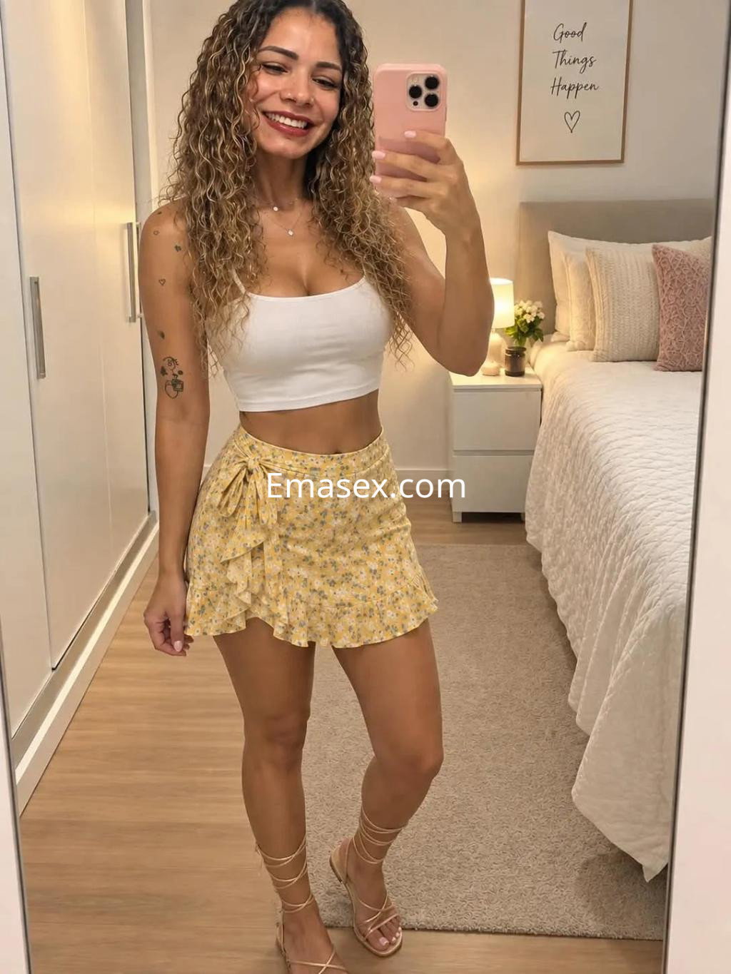 La escort en Zaragoza lleva una blusa blanca y una falda amarilla con flores, sonriendo en un ambiente interior.