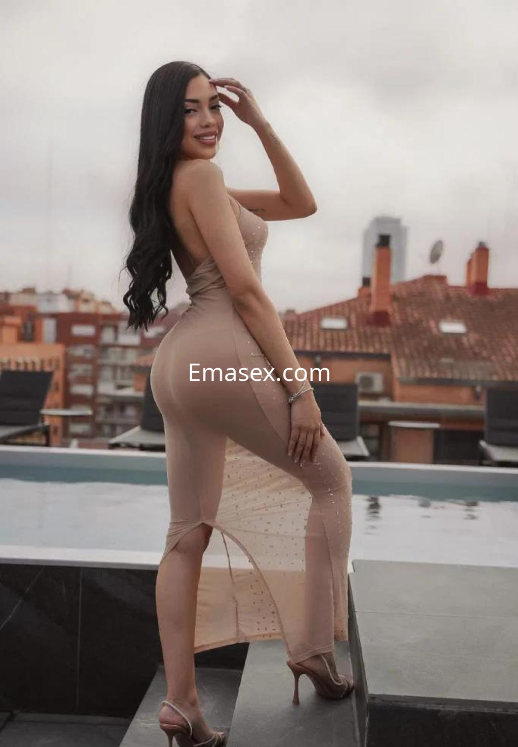 Escort en Tenerife, posando de perfil con un vestido largo y ajustado, mostrando su cabello largo y ondulado.