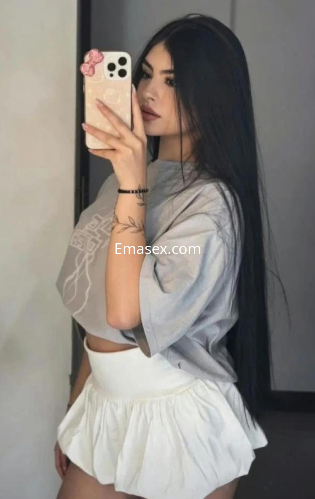 La puta se fotografía en un espejo, vistiendo una camiseta gris y una falda corta blanca en Barcelona.