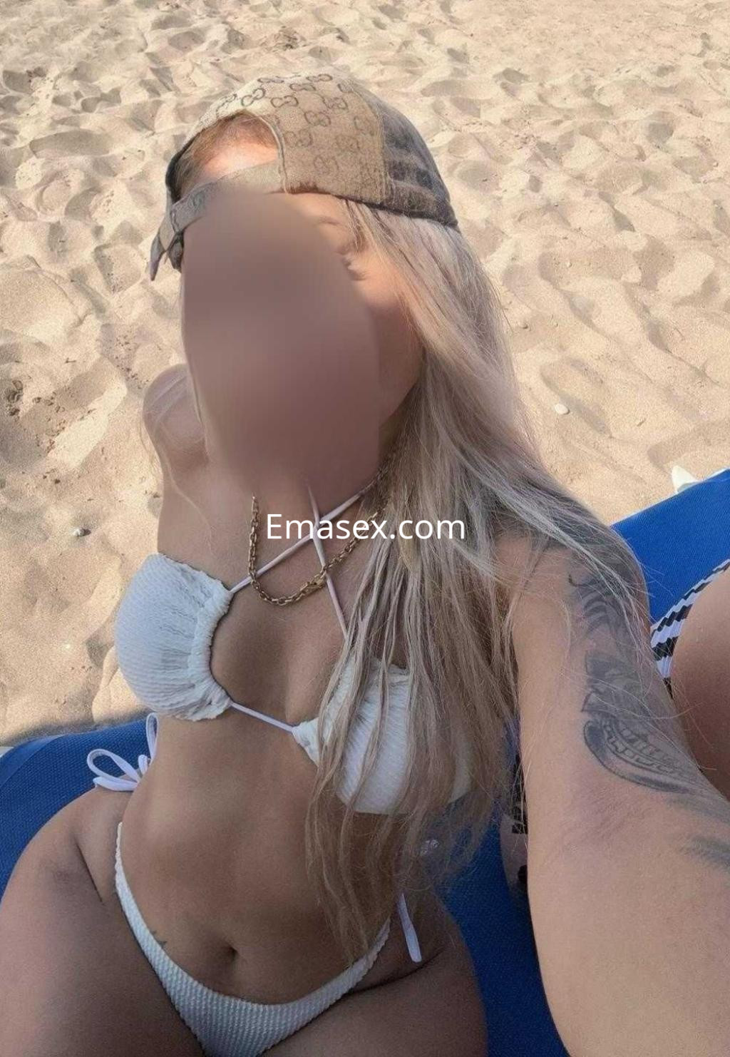 Escort en Barcelona con cabello largo y rubio, luciendo un bikini blanco en la playa durante un día soleado.