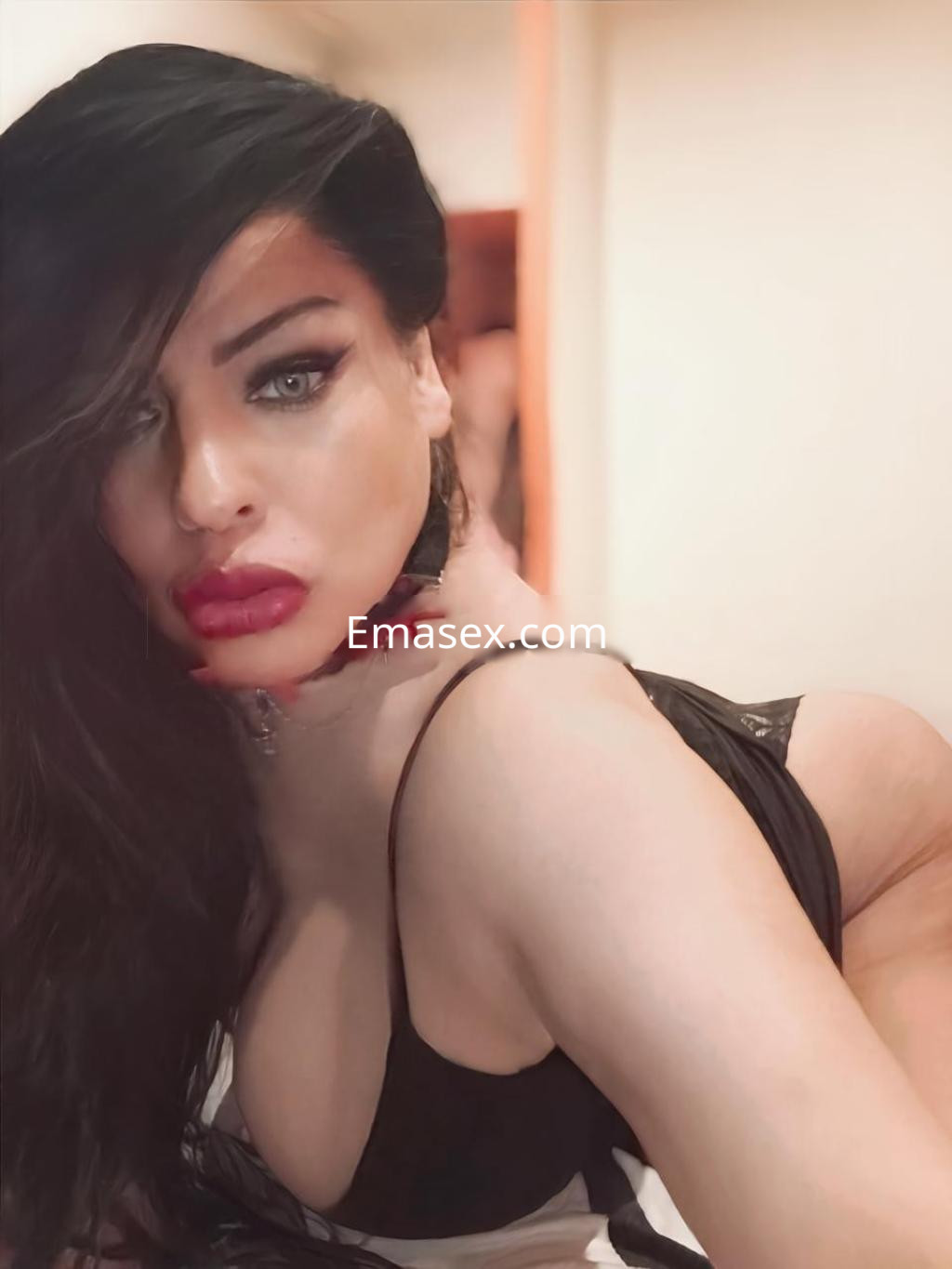 La puta en Barcelona luce un vestido negro ajustado, con cabello largo y oscuro, posando con una mirada seductora.