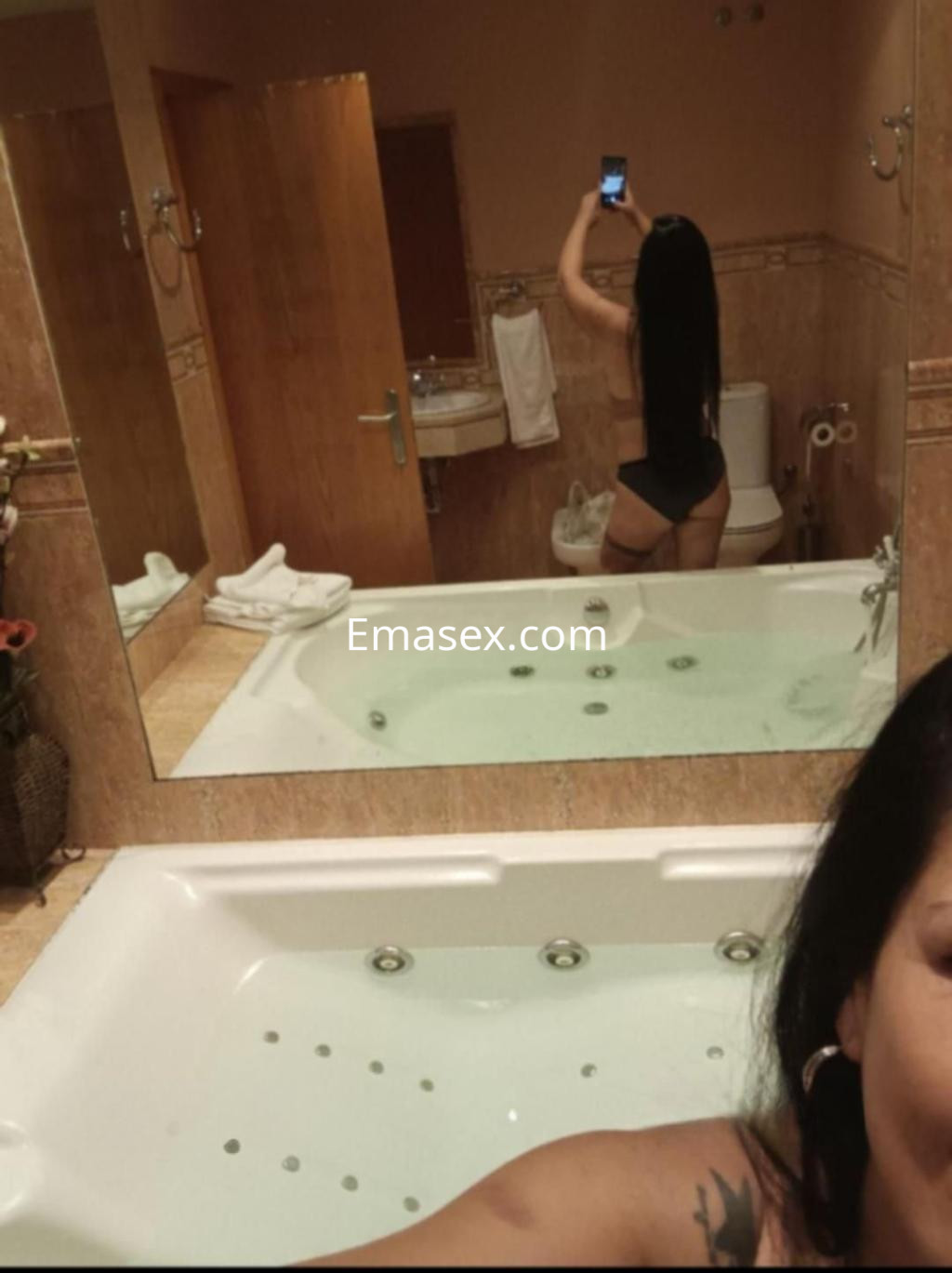 Escort en Sevilla toma una selfie frente a un jacuzzi, luciendo un atuendo negro y cabello largo y oscuro.