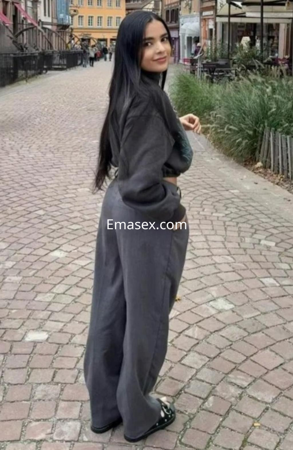 Escort en Zaragoza vistiendo un conjunto gris de sudadera y pantalones amplios, sonriendo en una calle empedrada.