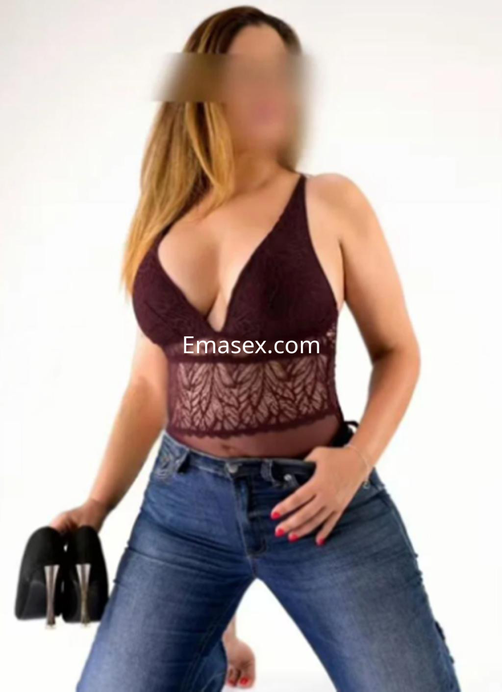 Escort con cabello largo y lacio, vistiendo un top de encaje burdeos y jeans ajustados en un fondo neutro de Santander.