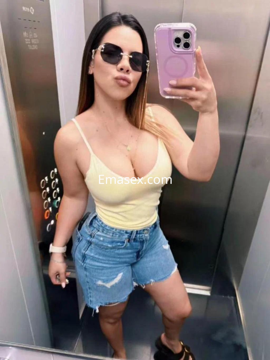 Escort en Palma de Mallorca, luciendo una camiseta amarilla sin mangas y shorts de mezclilla, con gafas de sol.