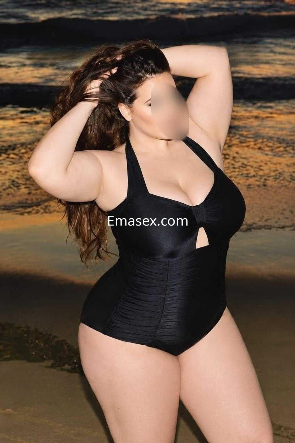 Puta de Badajoz posa en la playa con un traje de baño negro, mostrando su cabello rizado y su figura curvilínea.