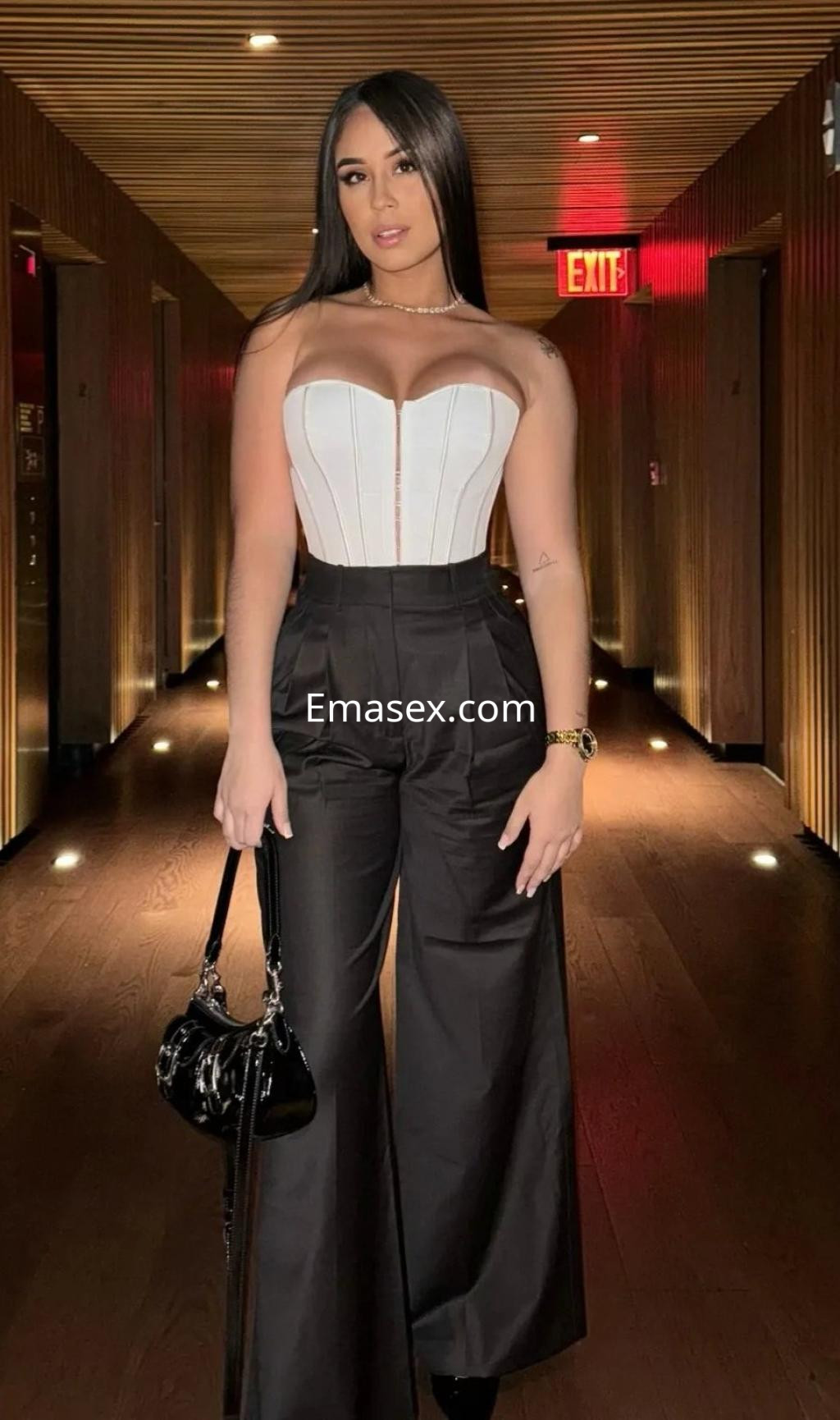 La puta se muestra en Zaragoza, vistiendo un corset blanco y pantalones negros amplios, en un pasillo elegante.