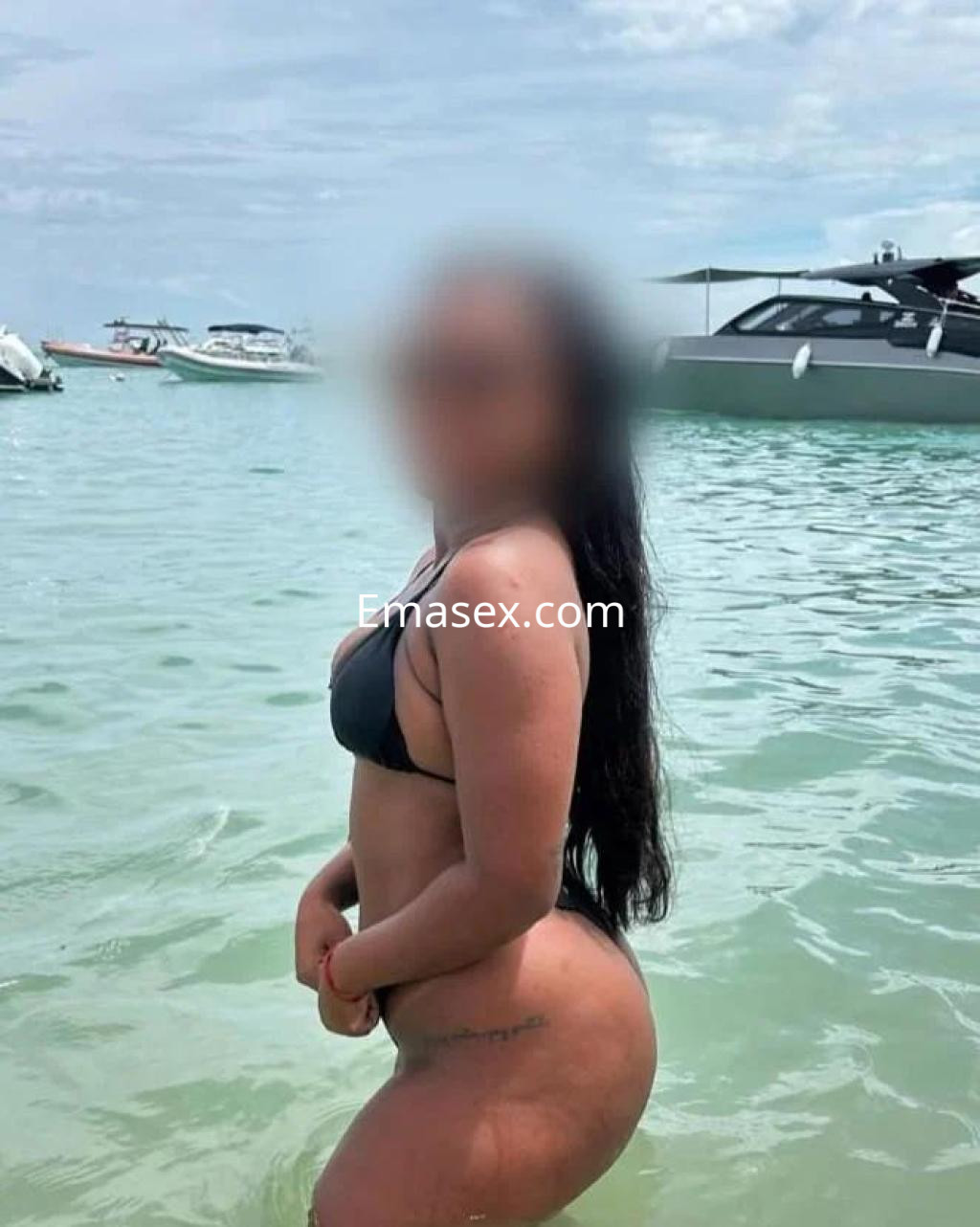 Puta en Girona con bikini negro, posando en el agua con cabello largo y ondulado, mostrando una figura curvilínea.