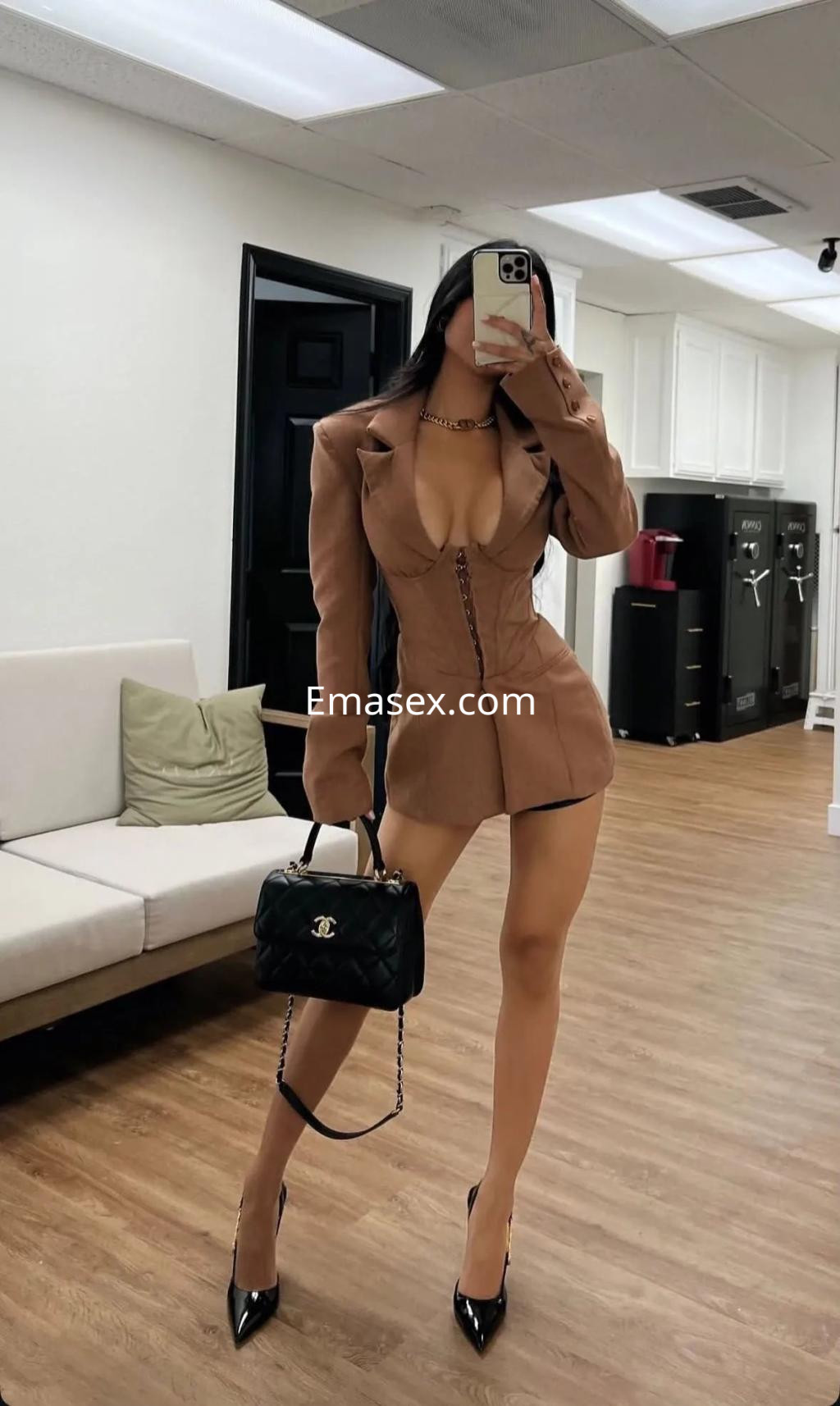 Escort en Palma de Mallorca, vistiendo un vestido marrón ajustado y tacones altos, posando en un interior moderno.