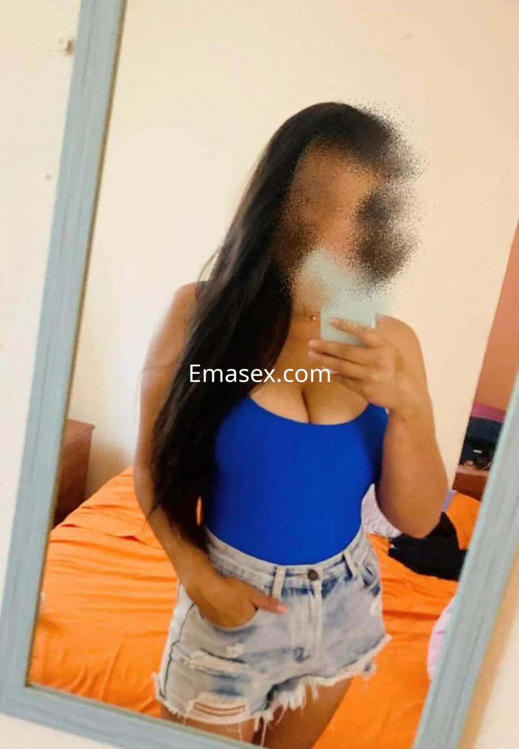 Puta con cabello largo y oscuro, viste un traje de baño azul y shorts de mezclilla, posando frente a un espejo en Valladolid.