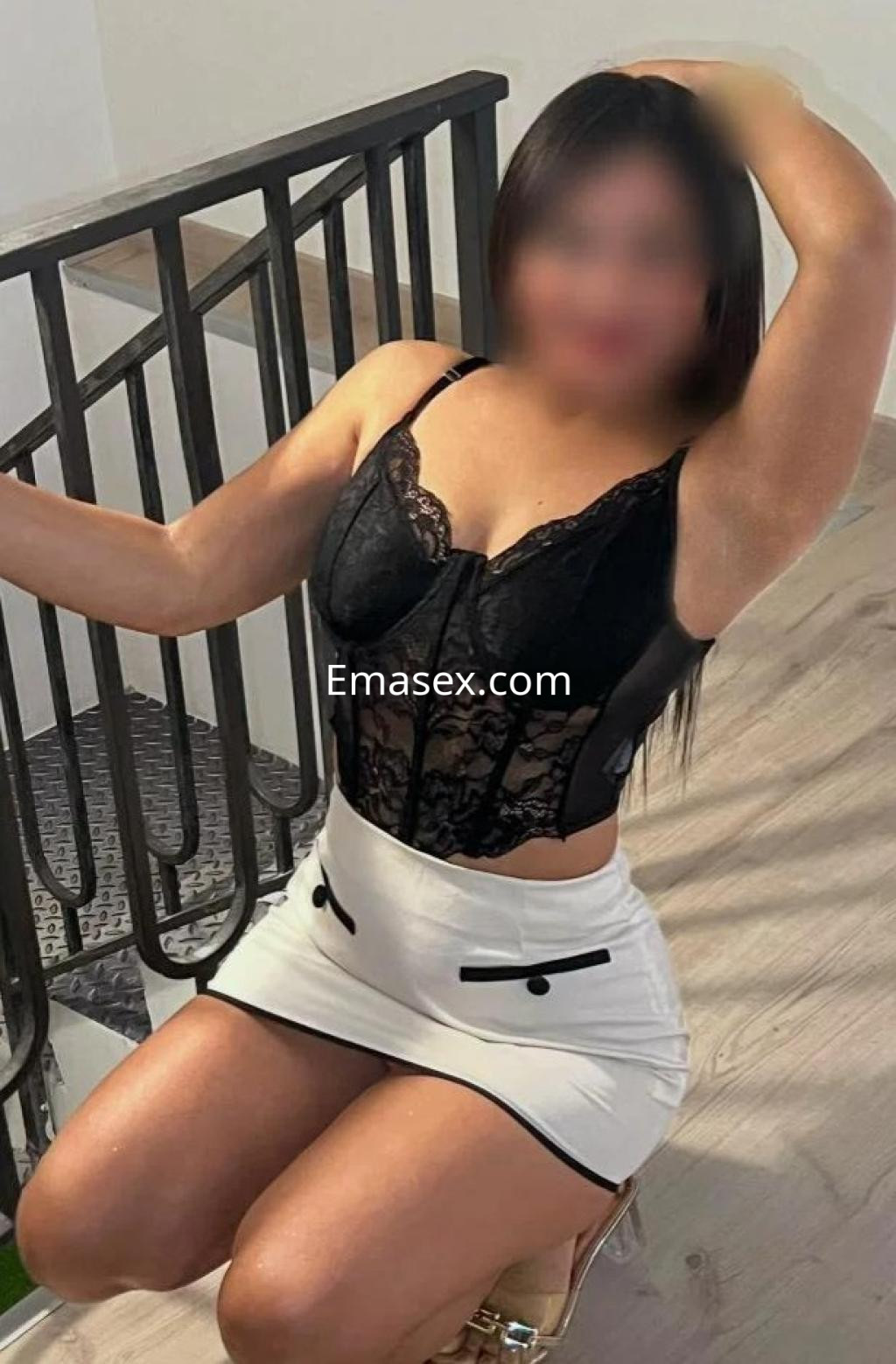 Puta en Castellón vistiendo un corset negro de encaje y una falda corta blanca, posando de rodillas en una escalera.