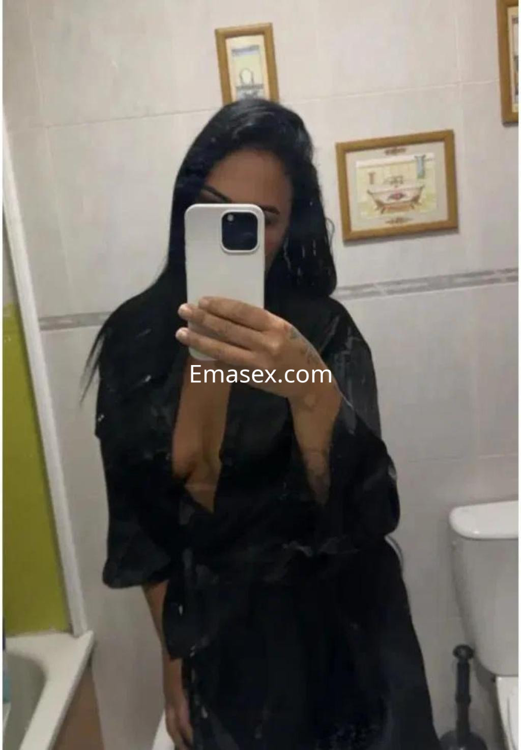 Escort en Toledo con cabello oscuro, vistiendo una bata negra y posando mientras se mira en un espejo.